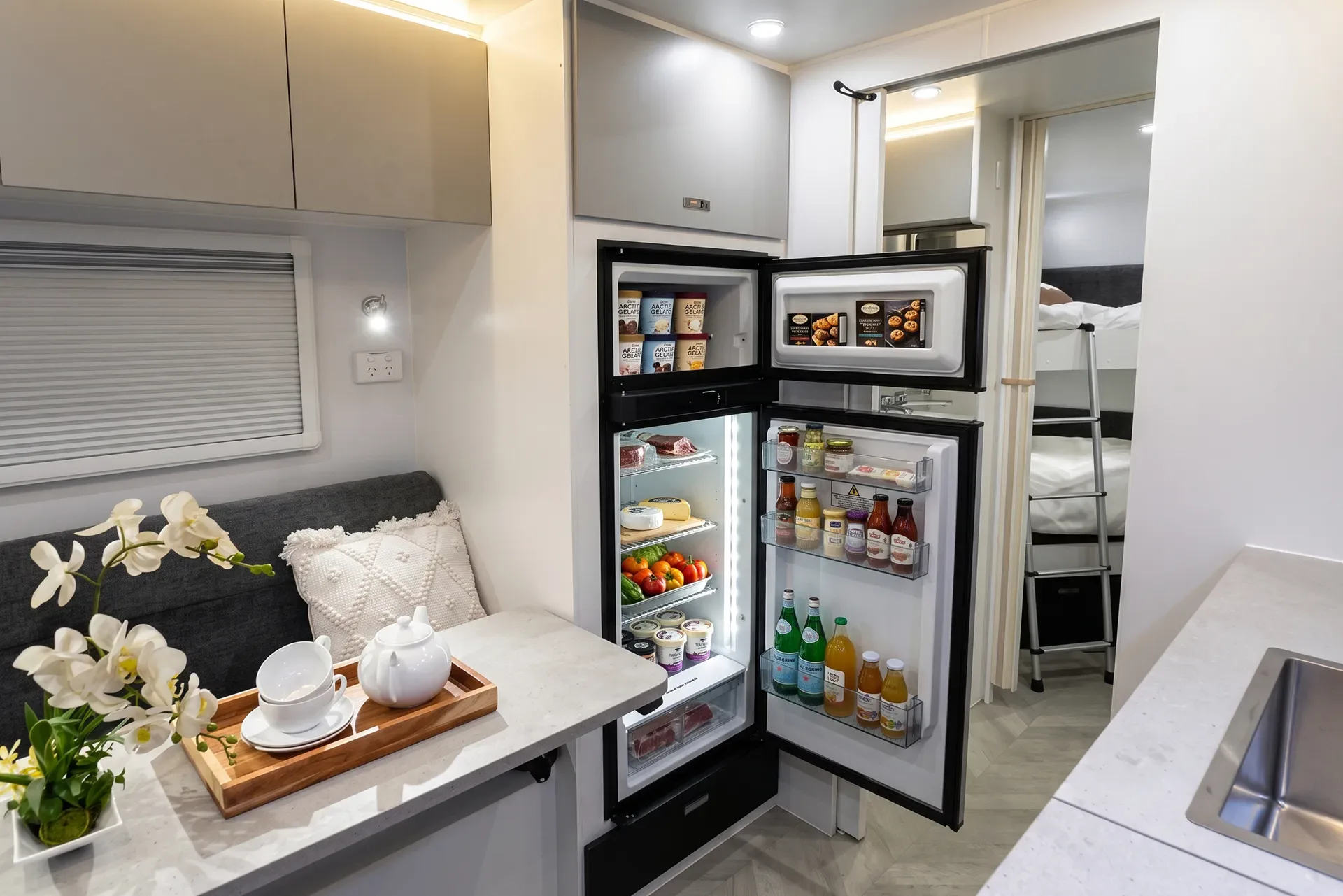 Galley and dinette: timber table, upholstered lounge, kitchen bench with cooktop and microwave, ensuite beyond