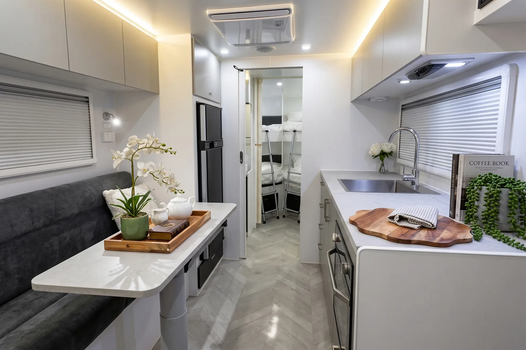 Caravan interior looking toward the bed: CNC cabinetry, waterfall benchtop and floor, bush through the windows